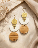 Kazuri brass and wood statement earrings laid flat on a textured stone surface alongside dried flowers and neutral linen fabric
