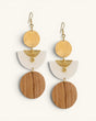 Kazuri brass and wood statement earrings shown as a pair, with hammered disc, white half-moon, and wood circle tiers on cream background