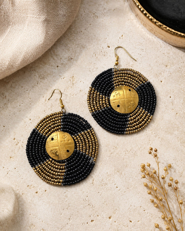 Kenyan hand-beaded circle earrings with alternating black and gold bead rows and engraved brass shilling center, styled product view