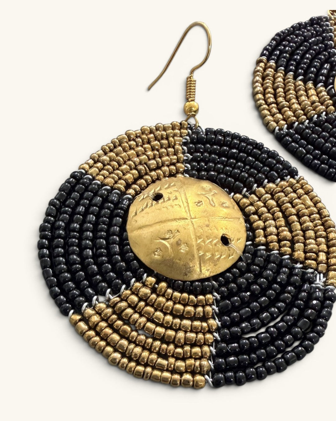 Close-up detail of Kenyan beaded circle earring showing alternating black and brass seed bead rows encircling engraved brass shilling