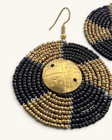 Close-up detail of Kenyan beaded circle earring showing alternating black and brass seed bead rows encircling engraved brass shilling
