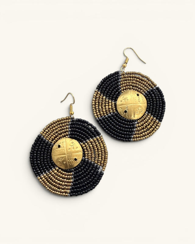 Pair of Kenyan hand-beaded circle earrings flat lay showing black and gold bead pattern with brass shilling centerpieces