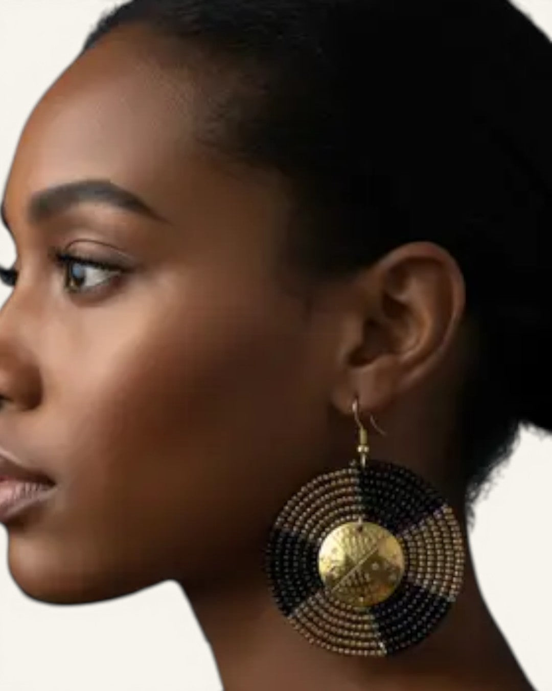Kenyan beaded circle earring worn on model ear in close side profile, brass shilling coin center visible against layered black beads