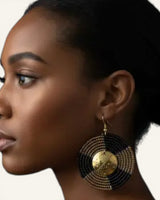 Kenyan beaded circle earring worn on model ear in close side profile, brass shilling coin center visible against layered black beads