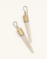 Pair of hand-carved bone spike dangle earrings with brass caps angled on white background showing natural surface texture