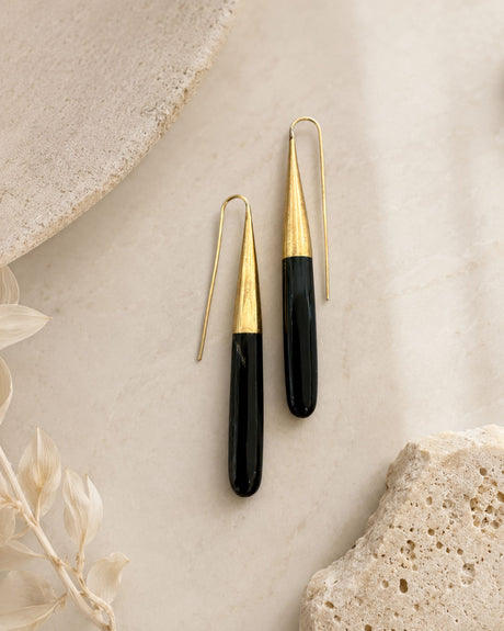 Kanai Kenyan hand-carved horn and brass threader earrings styled on marble surface with dried botanicals, front view
