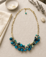 Blue beaded textile necklace draped on a vanity surface with soft lifestyle styling