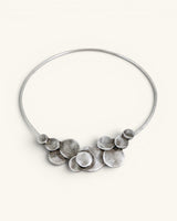 Silver-plated pewter collar necklace with stacked disc cluster centered at front, shown on off-white background