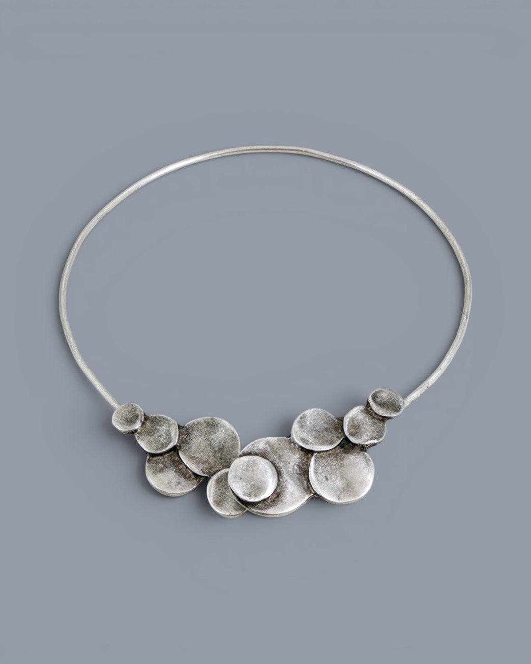 Silver-plated pewter collar necklace with layered disc cluster at center front, photographed on a gray background