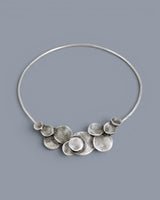 Silver-plated pewter collar necklace with layered disc cluster at center front, photographed on a gray background