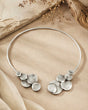 Pewter collar necklace with disc clusters at both open ends, laid flat on a sandy stone surface with dried botanicals