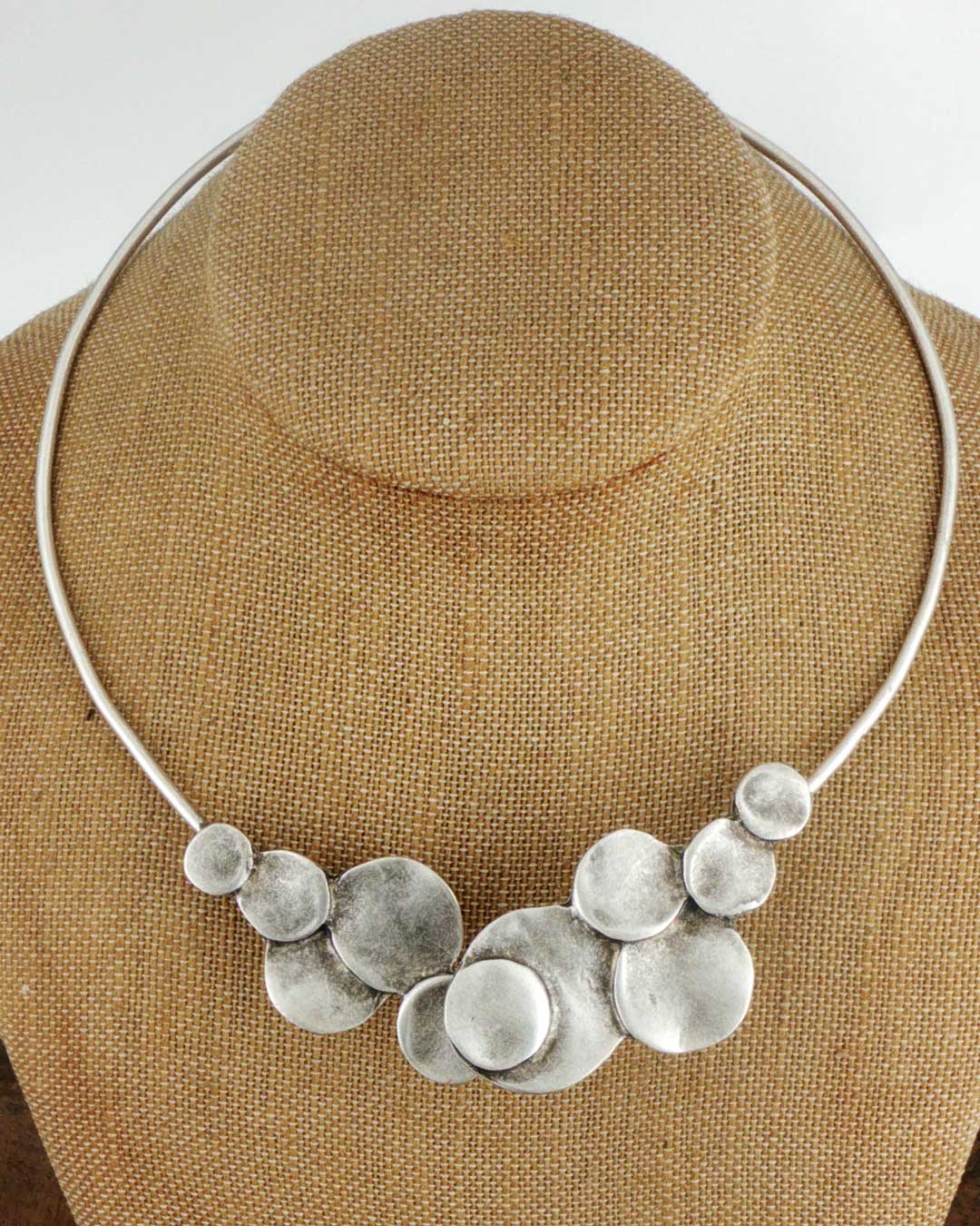 Silver-plated pewter collar necklace with stacked disc cluster at center front, displayed on a burlap jewelry bust