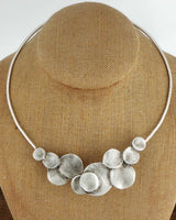 Silver-plated pewter collar necklace with stacked disc cluster at center front, displayed on a burlap jewelry bust