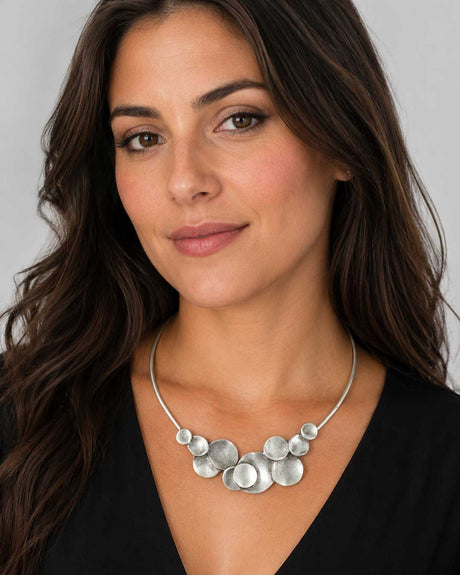 Silver-plated pewter collar necklace with stacked disc cluster worn by a brunette model in a black v-neck top
