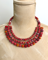 Red textile-wrapped bead layered bib necklace draped on a wooden dress form showing natural drape and mixed red bead rows