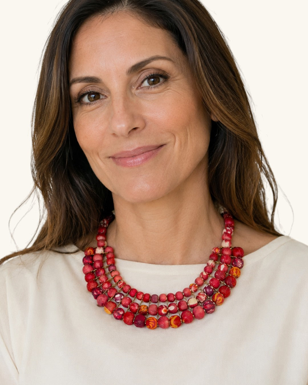 Red textile-wrapped bead layered bib necklace worn by a model in a cream top, close-up showing three rows at the neckline