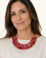 Red textile-wrapped bead layered bib necklace worn by a model in a cream top, close-up showing three rows at the neckline