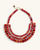 Red textile-wrapped bead layered bib necklace flat lay, four rows of mixed red beads with gold wire connectors and clasp