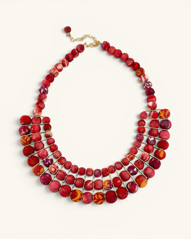 Red textile-wrapped bead layered bib necklace flat lay, four rows of mixed red beads with gold wire connectors and clasp