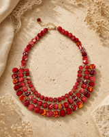 Red textile-wrapped bead layered bib necklace displayed on travertine surface
