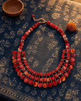 Red textile-wrapped beaded layered bib necklace on indigo fabric background with rim lighting