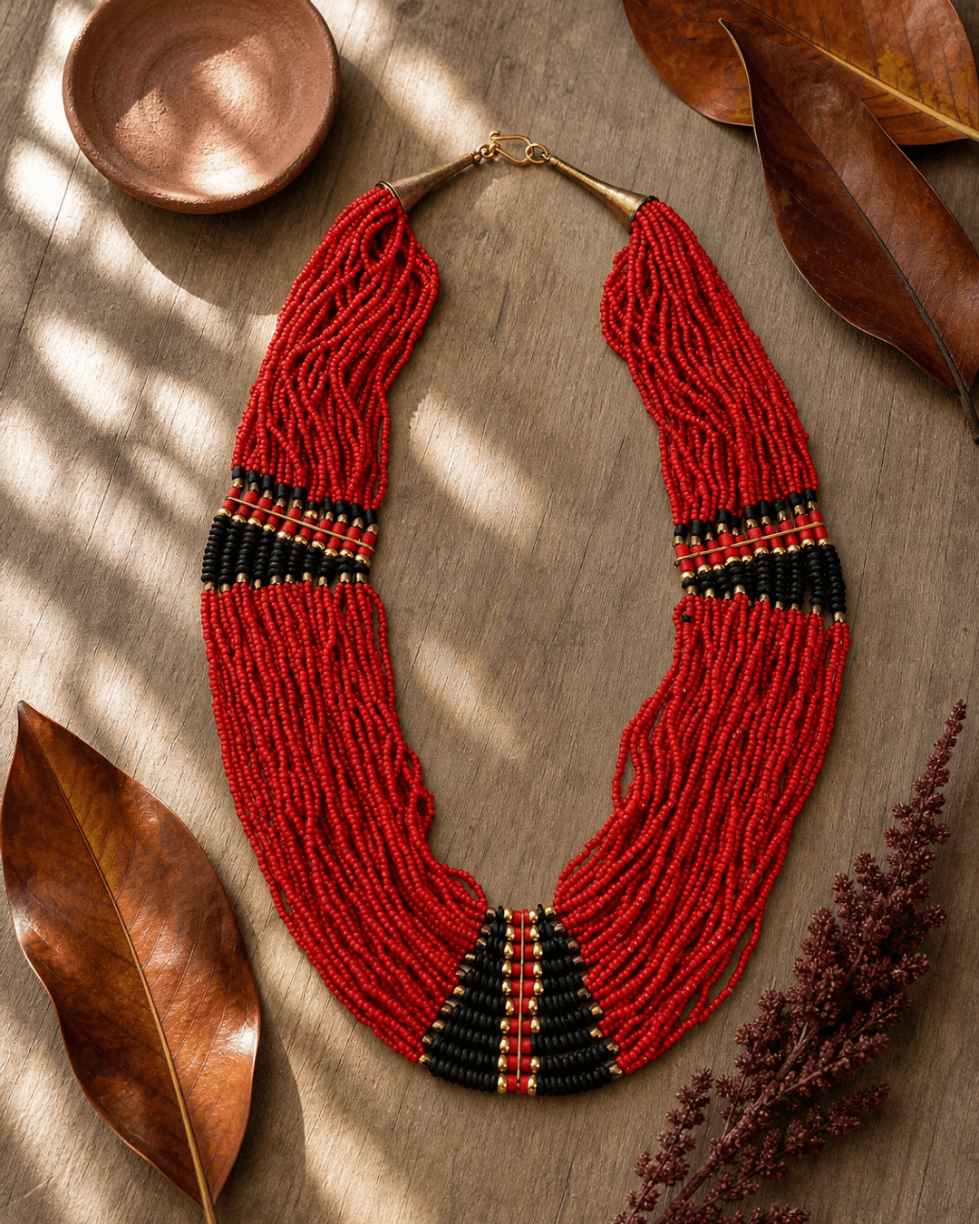 Red statement necklace with black beads on botanical flatlay with green leaves