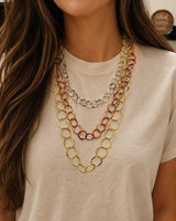 Three-strand mixed metal chain necklace worn close-up on a model's chest, with gold, copper, and silver circular link strands layered