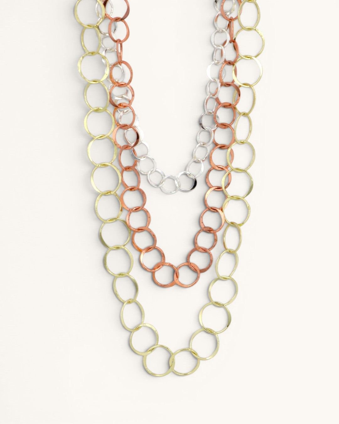 Three-strand mixed metal chain necklace close-up showing interlocked gold, copper, and silver circle links on white background