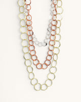 Three-strand mixed metal chain necklace close-up showing interlocked gold, copper, and silver circle links on white background