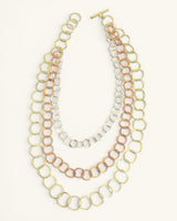 Three-strand mixed metal chain necklace laid flat on white background with all three circle-link strands and toggle bar clasp visible