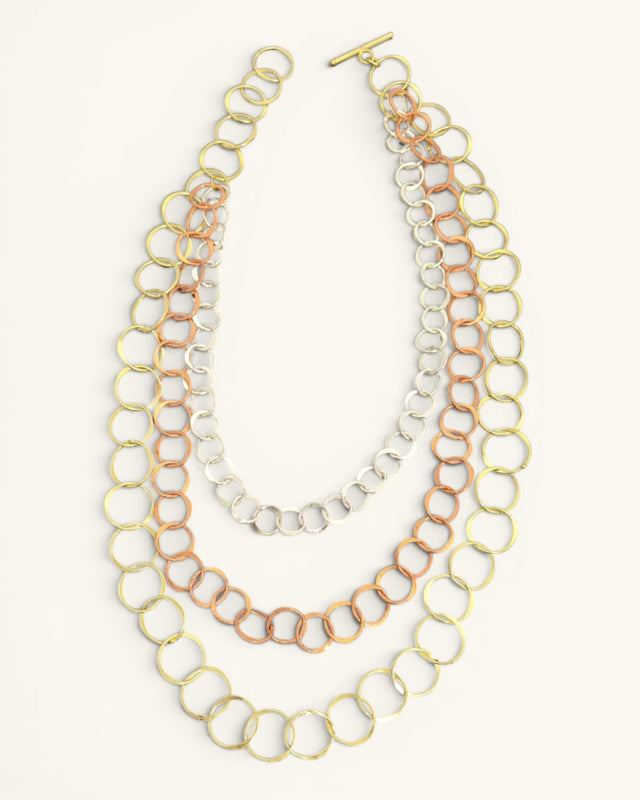 Three-strand mixed metal chain necklace laid flat on white background with all three circle-link strands and toggle bar clasp visible
