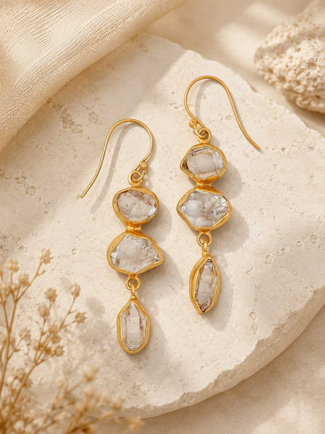Triple Herkimer quartz gold-plated drop earrings laid on a stone surface with dried flowers, styled lifestyle view