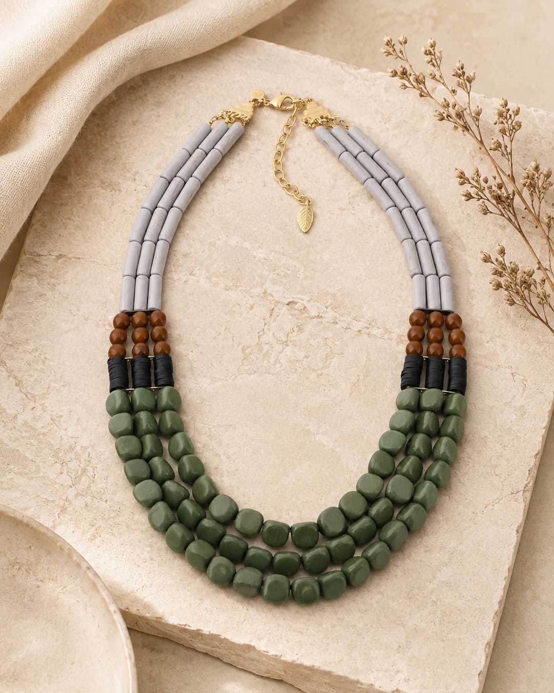 Triple strand magnesite, serpentine and vulcanite beaded necklace laid flat on a stone slab with linen fabric and dried botanicals