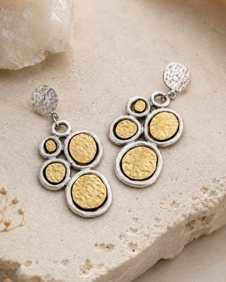 Turkish two-tone boho dangle earrings with hammered gold and silver discs, styled on stone surface with crystal