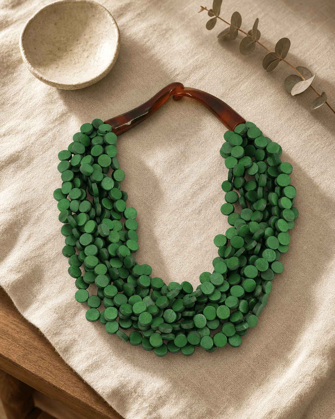 Twisted green wood disc pendant necklace on linen flatlay with journal