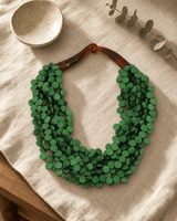 Twisted green wood disc pendant necklace on linen flatlay with journal